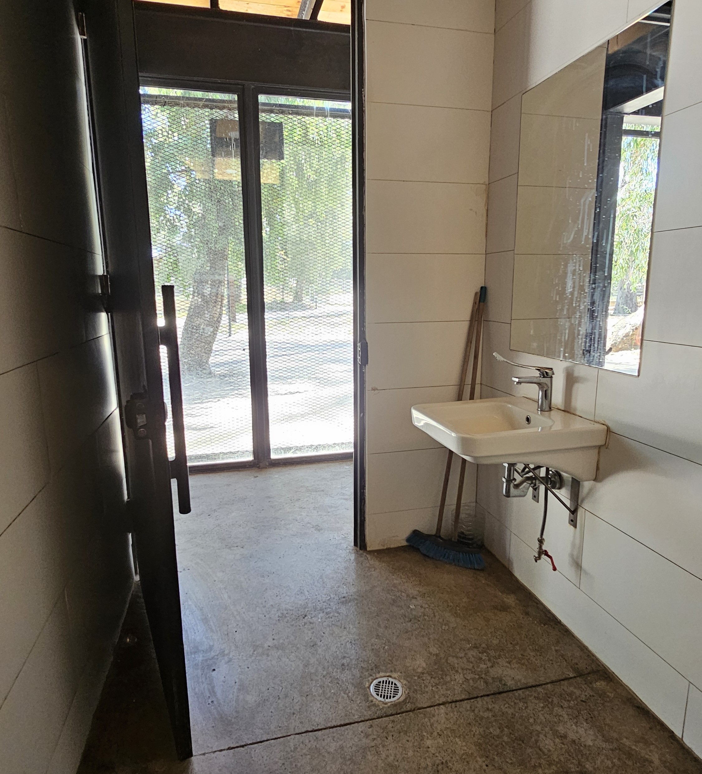 Ftografía del baño desde el interior, se aprecia el lavamanos accesible, espejo y la puerta amplia